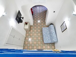 A room with patterned floor tiles, a white wardrobe, a small table with a vase, a blue patterned sofa, and a framed picture on the wall. - Appartamento a Vietri sul Mare ID 4144 (Vietri sul Mare)