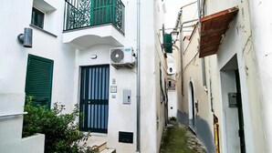 A narrow alleyway with a white building featuring a black door, green shutters, and a small balcony with a green railing. - Appartamento a Vietri sul Mare ID 4144 (Vietri sul Mare)