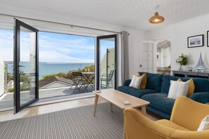 A modern living room with a large sliding glass door leading to a balcony with a view of the sea. - Glen View - Panoramic Sea Views (Saundersfoot)