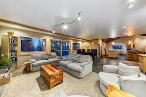 A modern living room with a sectional sofa, a wooden coffee table, and a fireplace. There are large windows offering a view of the outdoors.