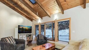Una sala de estar con sofá, sillones, una mesa de centro, televisor y ventanas amplias con vistas nevadas.