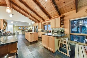Une cuisine spacieuse avec des poutres en bois, un grand îlot central et une vue sur l’extérieur.