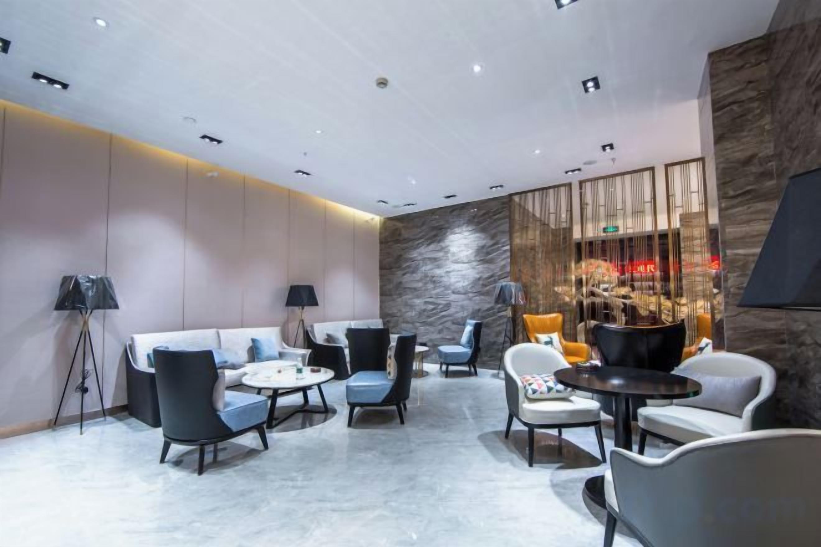 Un'elegante area lounge con divani, poltrone e tavolini, caratterizzata da una parete in pietra e illuminazione a incasso.