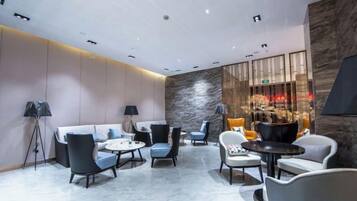 Un'elegante area lounge con divani, poltrone e tavolini, caratterizzata da una parete in pietra e illuminazione a incasso.