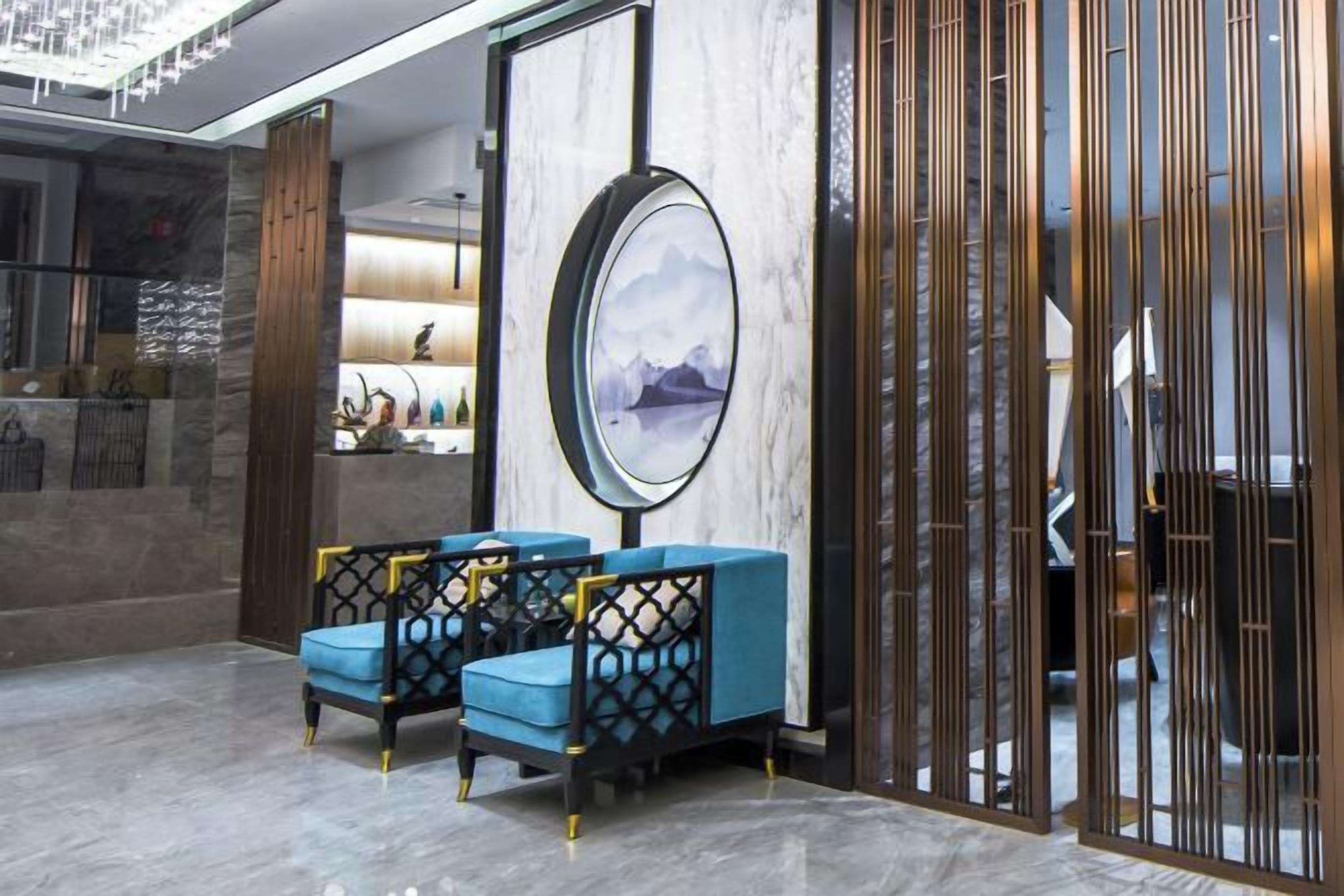 A lobby with a reception desk, seating area with blue chairs, a large framed artwork, and a decorative partition.