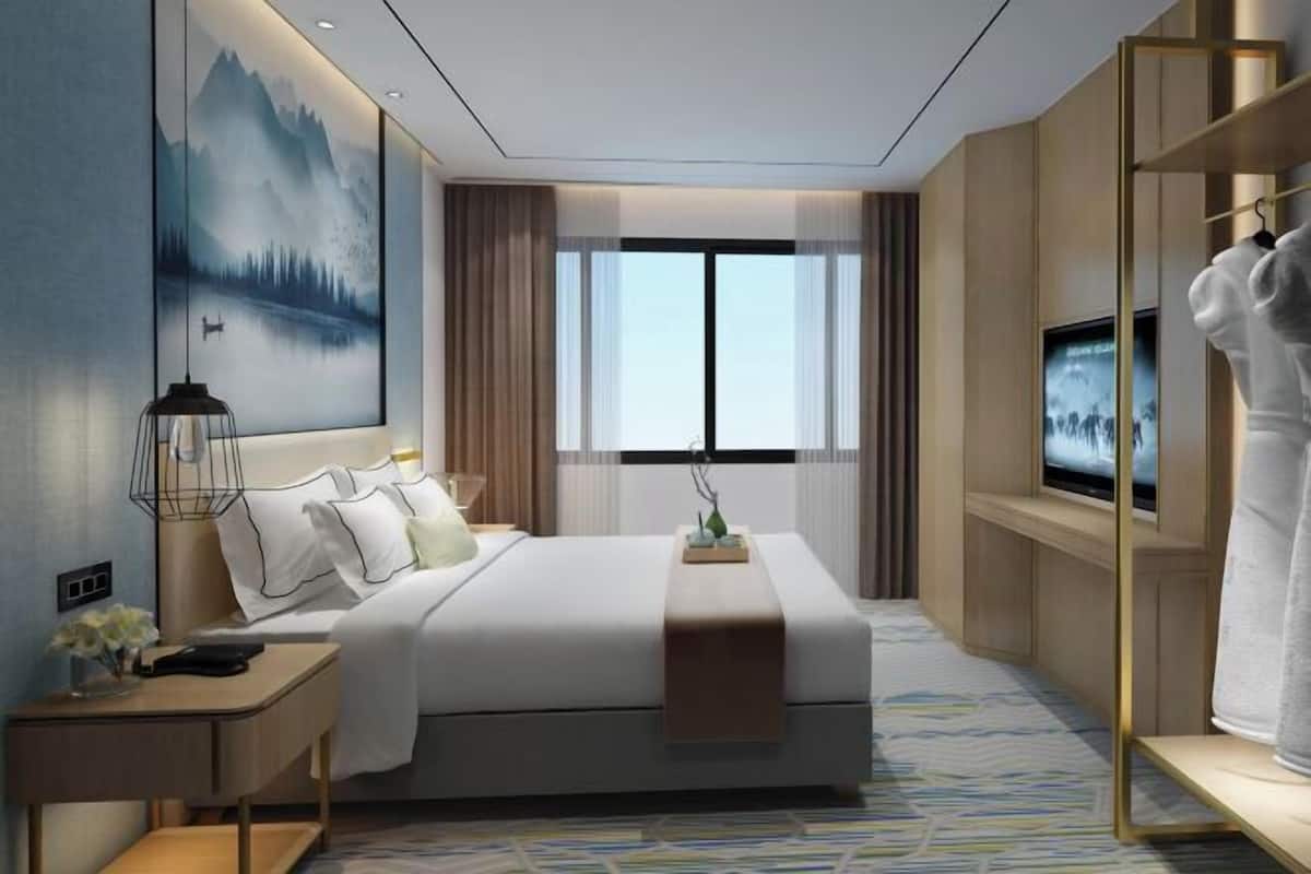 A modern hotel room with a large bed, a television, a desk, and a painting on the wall.