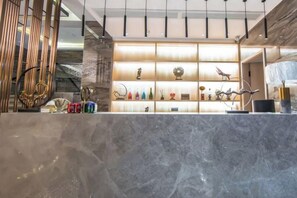 A reception area with a marble counter, shelves with decorative items, and a modern interior design. - Shangcheng Pusu Hotel (Wenzhou)