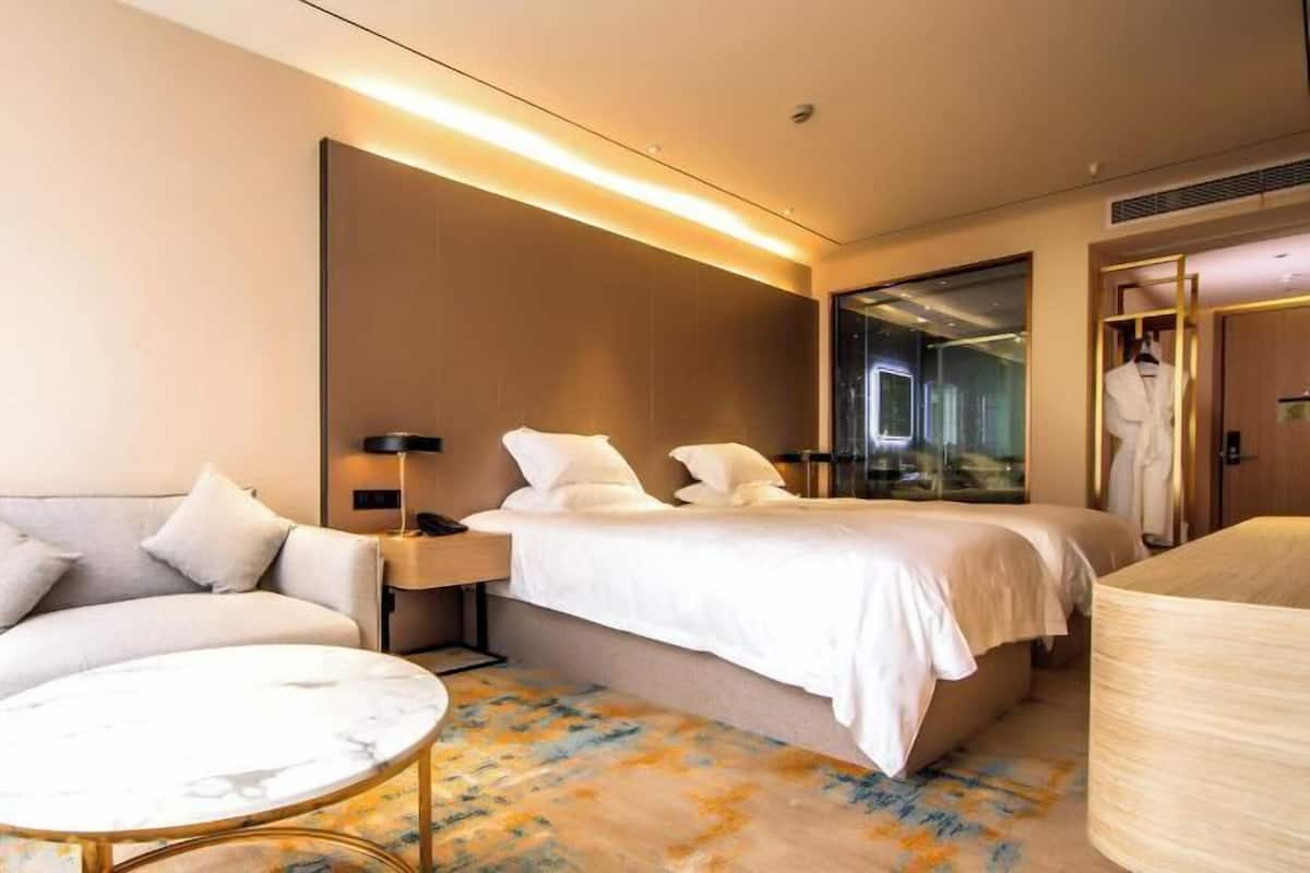A hotel room with a bed, a sofa, a round table, and a mirror.