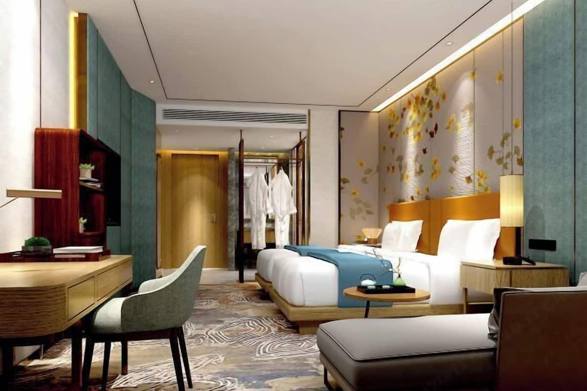 A modern hotel room with a bed, desk, chair, and a small table with a lamp.