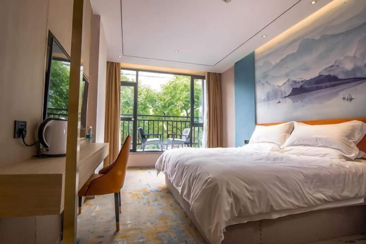 A hotel room with a bed, a desk, a chair, a large window, and a mural on the wall.