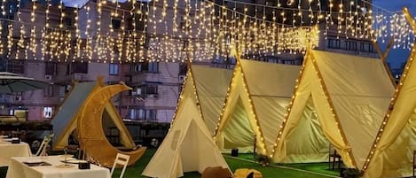 Una azotea con tiendas de campaña, mesas y luces colgantes.