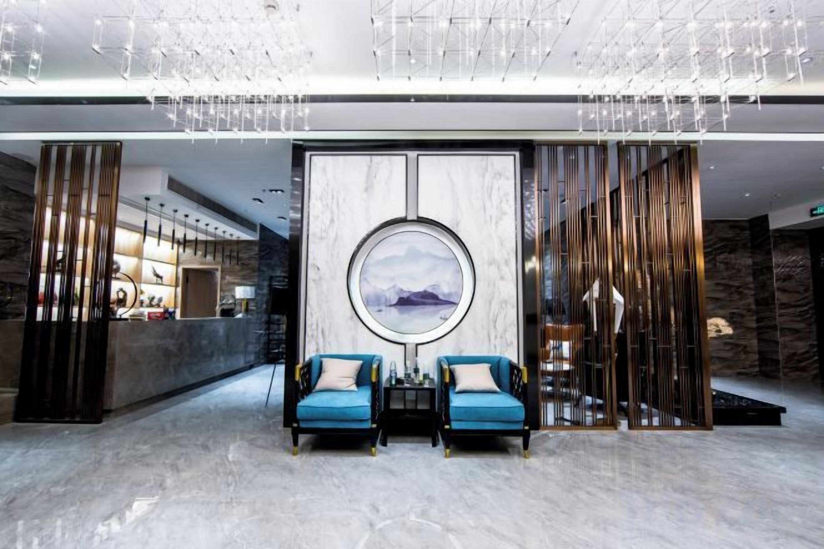 Una hall con una reception, due poltrone blu, un'opera d'arte circolare di grandi dimensioni e un lampadario moderno.