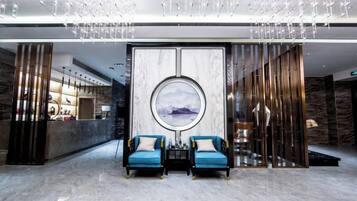 Una hall con una reception, due poltrone blu, un'opera d'arte circolare di grandi dimensioni e un lampadario moderno.