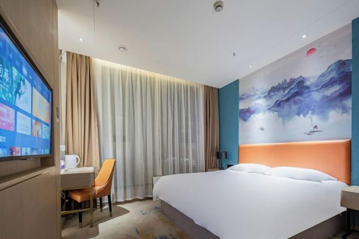 A hotel room with a bed, a desk with a chair, a television, and a painting on the wall.