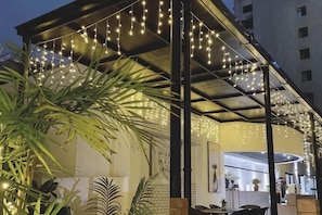 An outdoor seating area with string lights, potted plants, and a modern building in the background. - Shangcheng Pusu Hotel (Wenzhou)