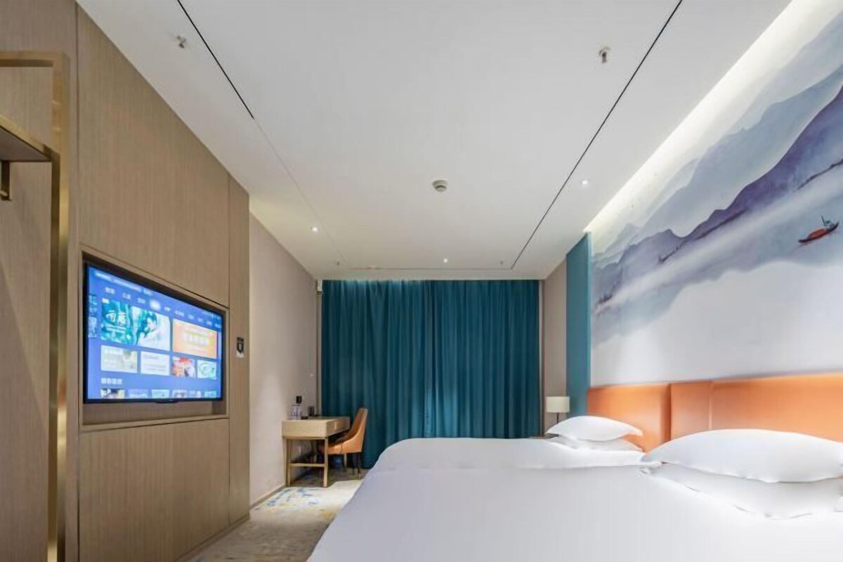 A hotel room with a bed, a desk, a TV, and a mural on the wall.