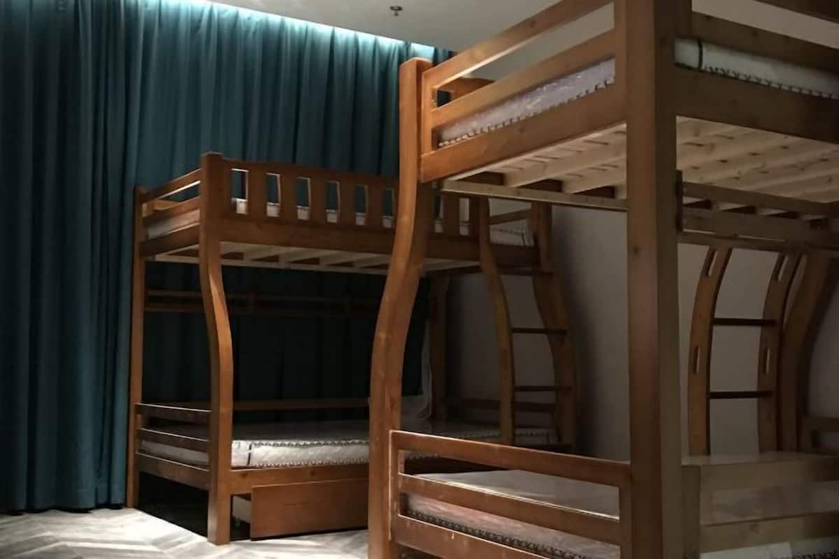 A bunk bed with a wooden frame and slatted design, a curtain, and a ceiling light fixture.