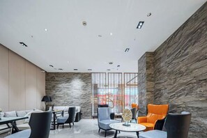 A modern hotel lobby with a marble floor, seating area with chairs and tables, and a stone accent wall. - Shangcheng Pusu Hotel (Wenzhou)