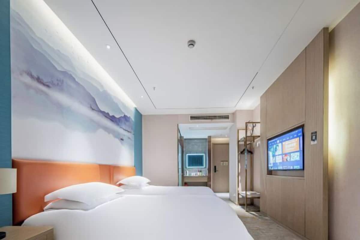 A hotel room with a large bed, a TV, and a wall mural.