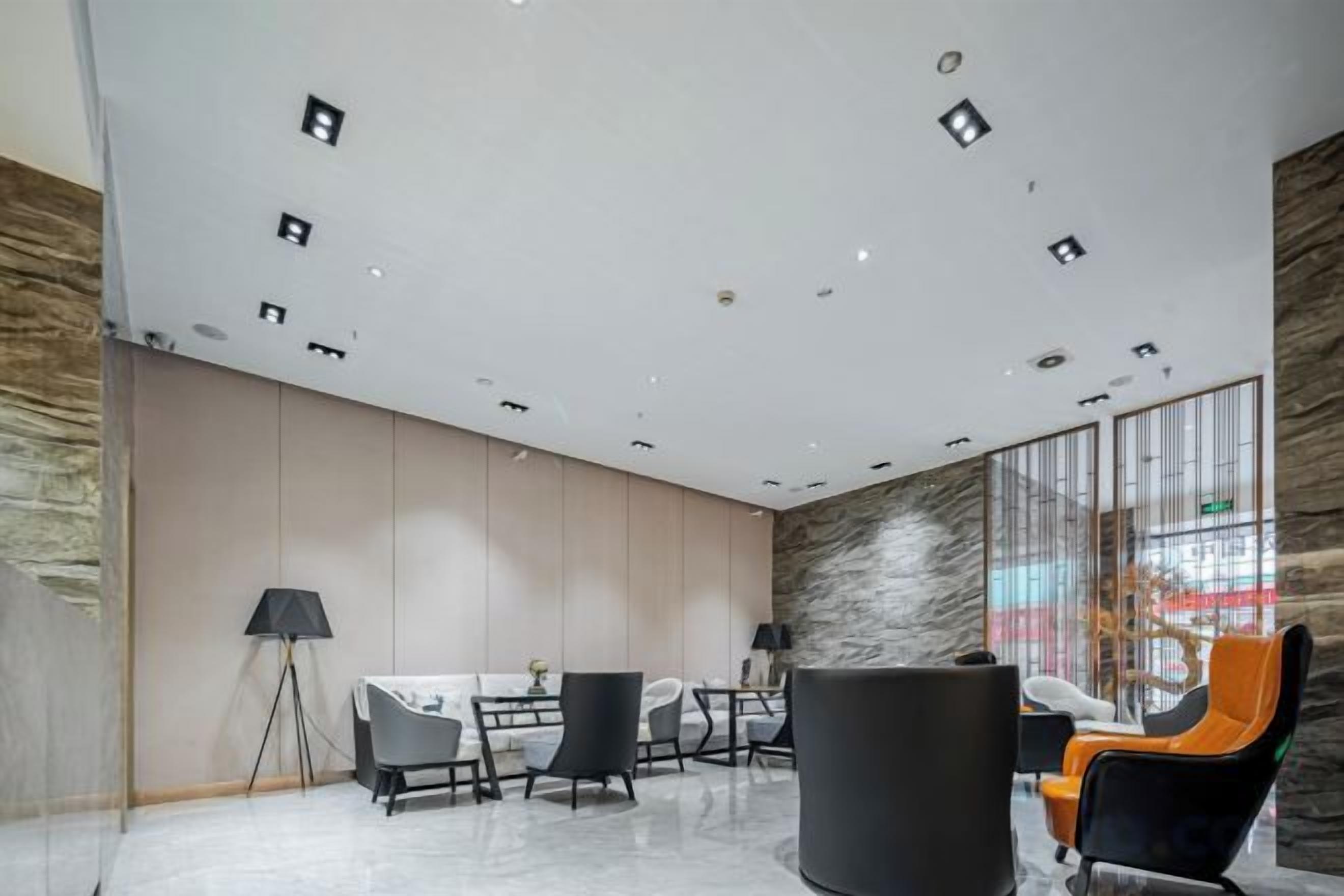 A modern interior with a high ceiling, recessed lighting, a marble floor, and a seating area with chairs and a table.