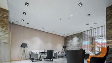 A modern interior with a high ceiling, recessed lighting, a marble floor, and a seating area with chairs and a table.