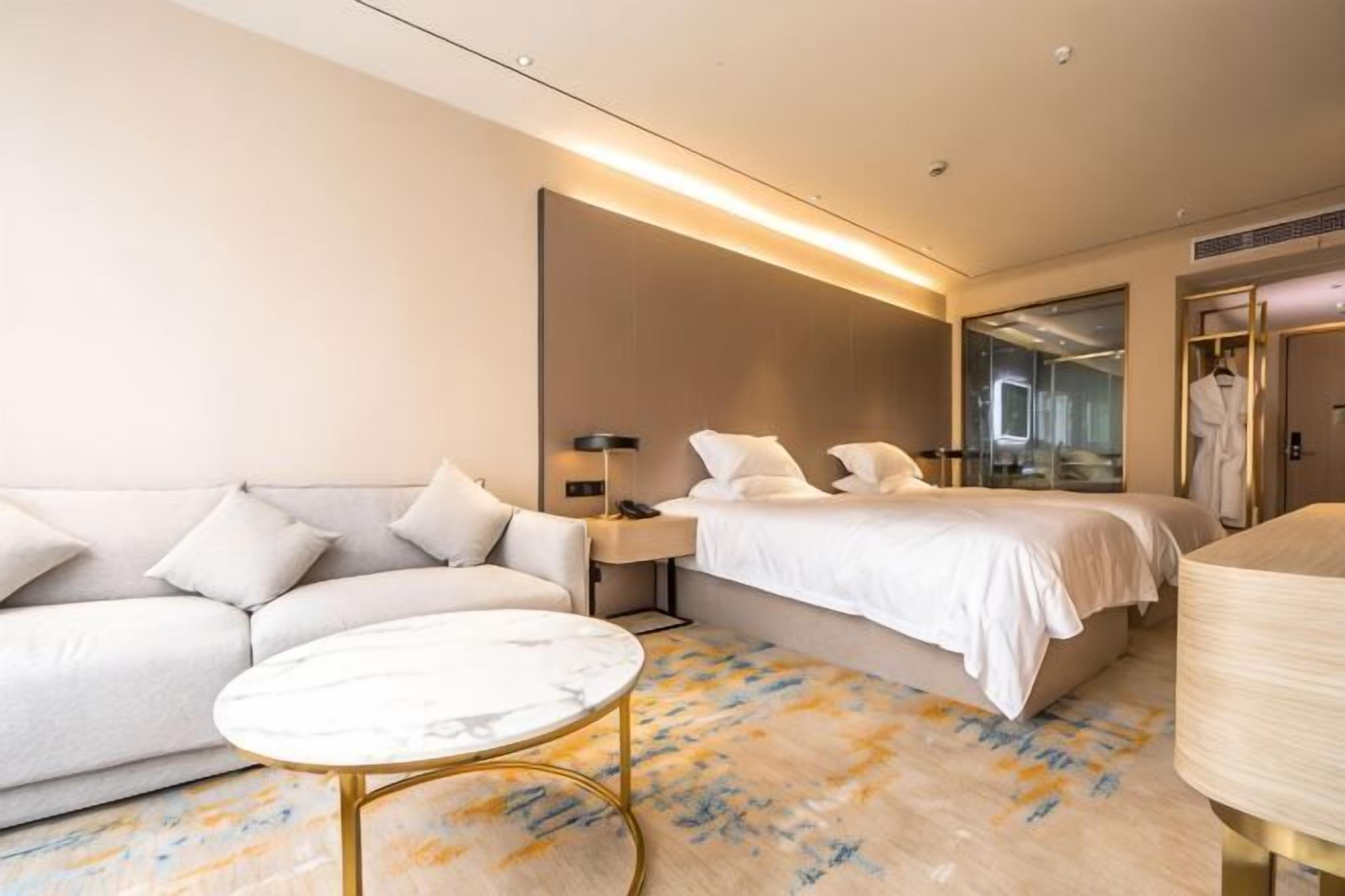 A hotel room with a sofa, a bed, a bedside table, a lamp, and a mirror.