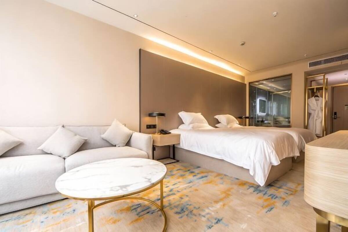 A hotel room with a sofa, a bed, a bedside table, a lamp, and a mirror.