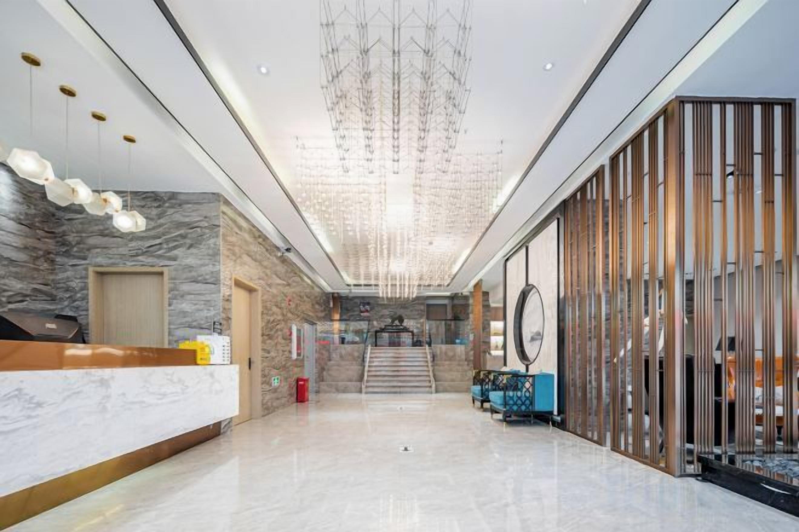 A hotel lobby with a reception desk, a staircase, and a modern chandelier.