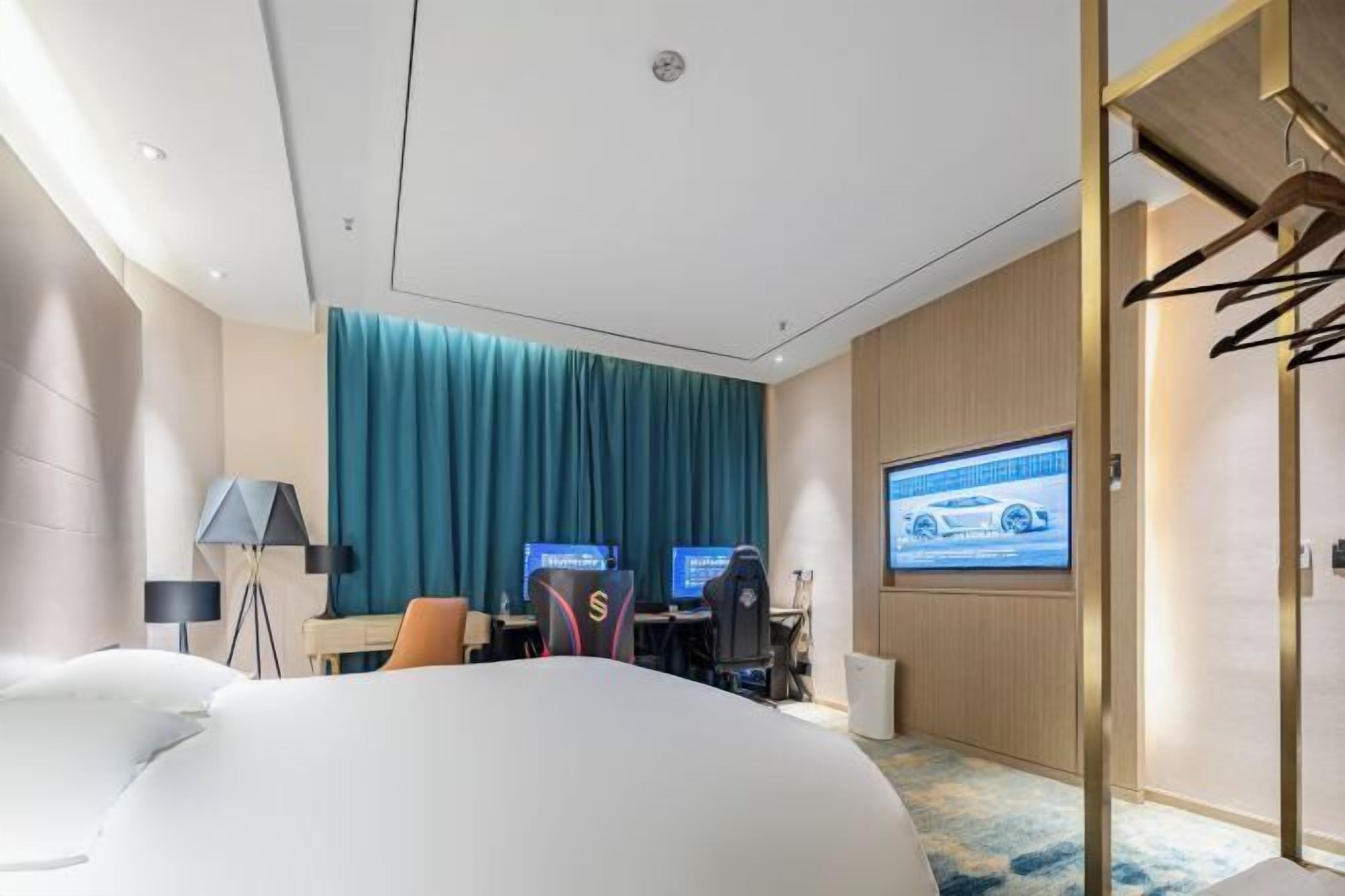 Een hotelkamer met een bed, een bureau met twee monitoren, een projectiescherm en een kledingkast.
