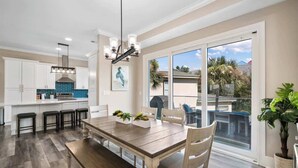 A modern kitchen with white cabinets, a blue backsplash, and a dining area with a wooden table and chairs. - Coastal Villas (Destin)