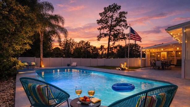 Une piscine avec des chaises et une table, un drapeau américain et un coucher de soleil.