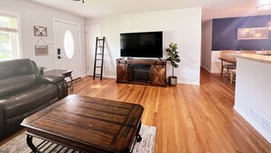 Un salon avec une table basse en bois, un canapé en cuir noir, un téléviseur posé sur un meuble en bois et un ventilateur de plafond.