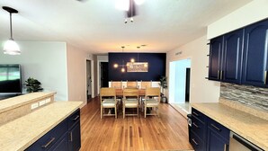 Une cuisine moderne avec des meubles en bois, un coin repas comprenant une table et des chaises, et un ventilateur de plafond.