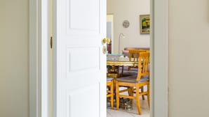 Una habitación con una puerta blanca, una mesa de comedor con sillas, una lámpara y un cuadro en la pared.