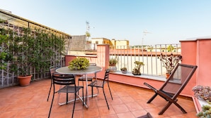 Terraza en la azotea con una mesa redonda, cuatro sillas y plantas en macetas.