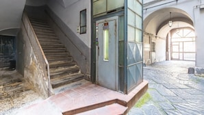 Una escalera conduce a una puerta con panel de vidrio, suelo de baldosas y techos abovedados.