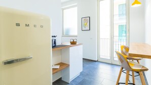 Eine kompakte Küche mit einem alten Smes-Kühlschrank, einer kleinen Holztheke und einem Essbereich mit einem gelben Stuhl.