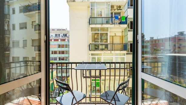 Ein Balkon mit zwei Stühlen und einem kleinen Tisch, mit Blick auf ein mehrgeschossiges Gebäude mit Balkonen und Fenstern.