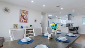 A modern dining area with a long table set for four, surrounded by chairs. A vase with flowers is on the table, and there is a painting on the wall. - Modern 4 Bed 2 Bath home with a pool, King bed sleeps 10 in Orlando close to UCF (Orlando)