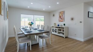 A dining area with a wooden table and white chairs, a white cabinet with decorative items, and a large window with a view of the outdoors. - Modern 4 Bed 2 Bath home with a pool, King bed sleeps 10 in Orlando close to UCF (Orlando)