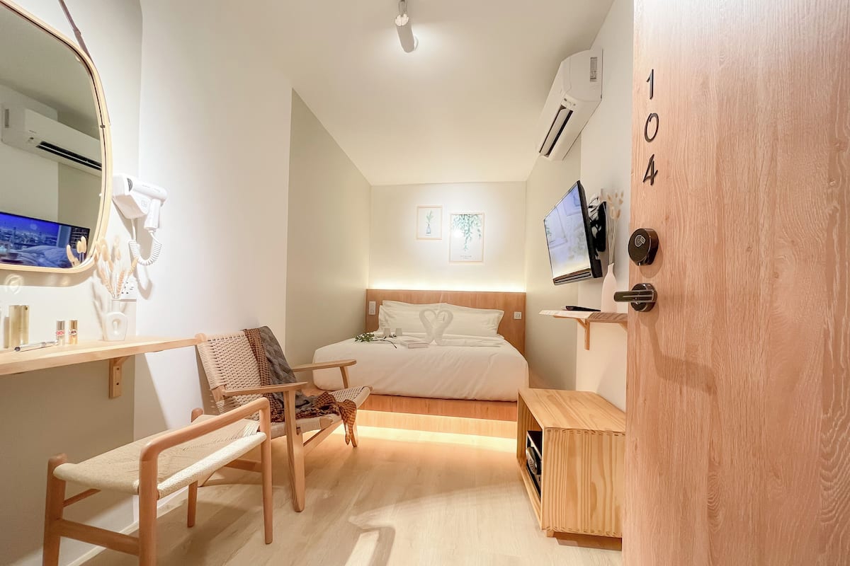 A modern hotel room with a bed, a desk, a chair, a TV, and an air conditioning unit.