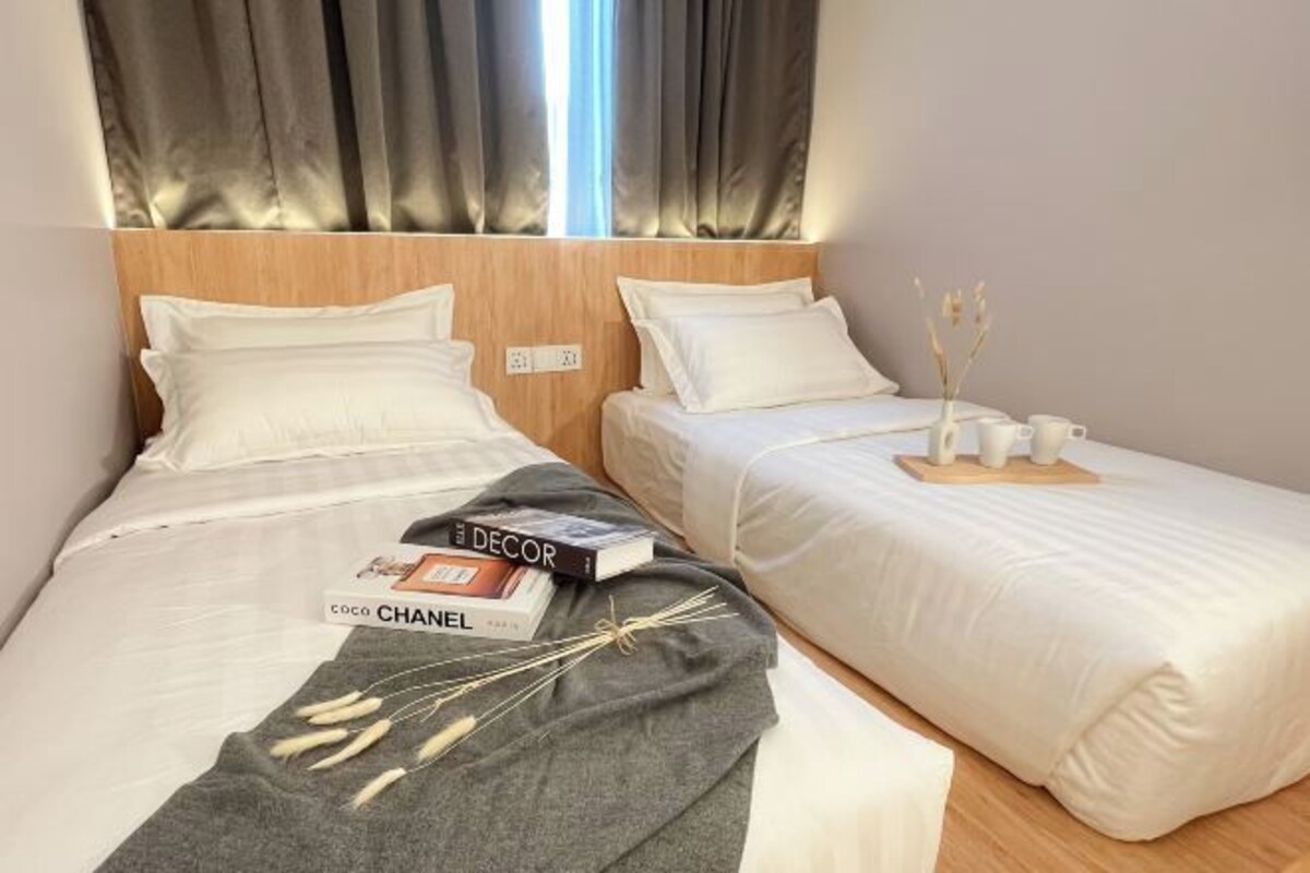 A hotel room with two beds, each with white bedding and a wooden headboard. There are books and a decorative branch on the bed.