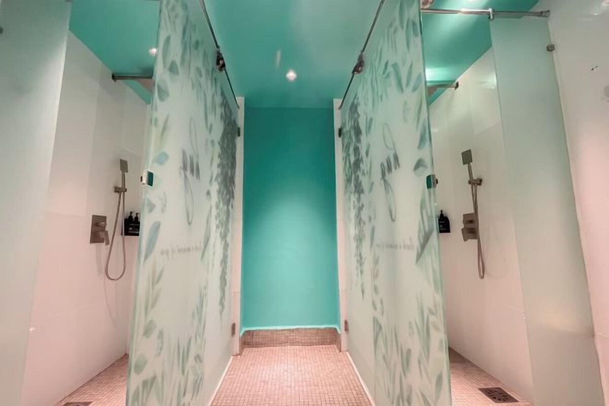 A modern bathroom with a teal accent wall, glass shower doors, and a tiled floor.