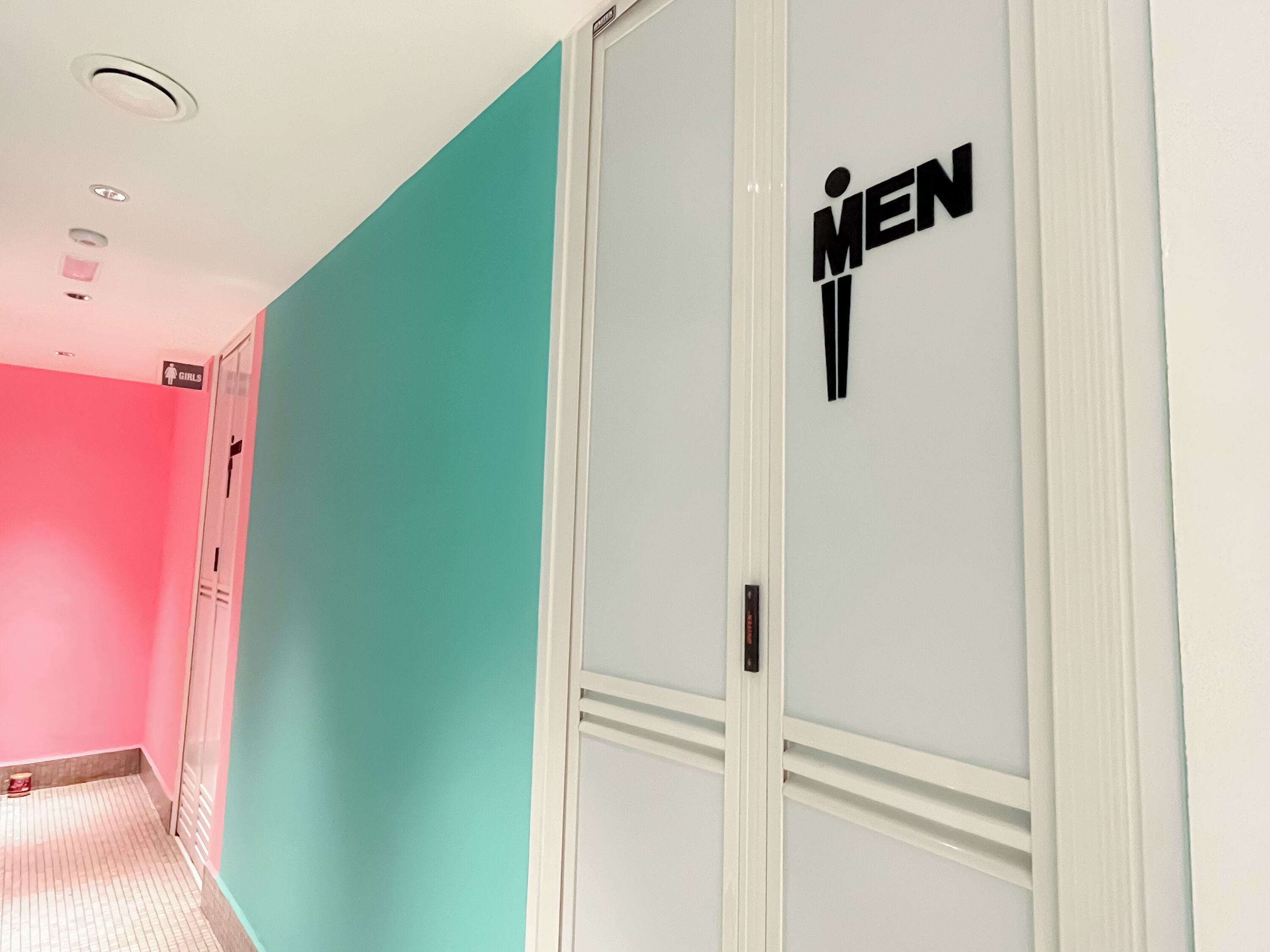 A hallway with a teal wall and a white door labeled "MEN".