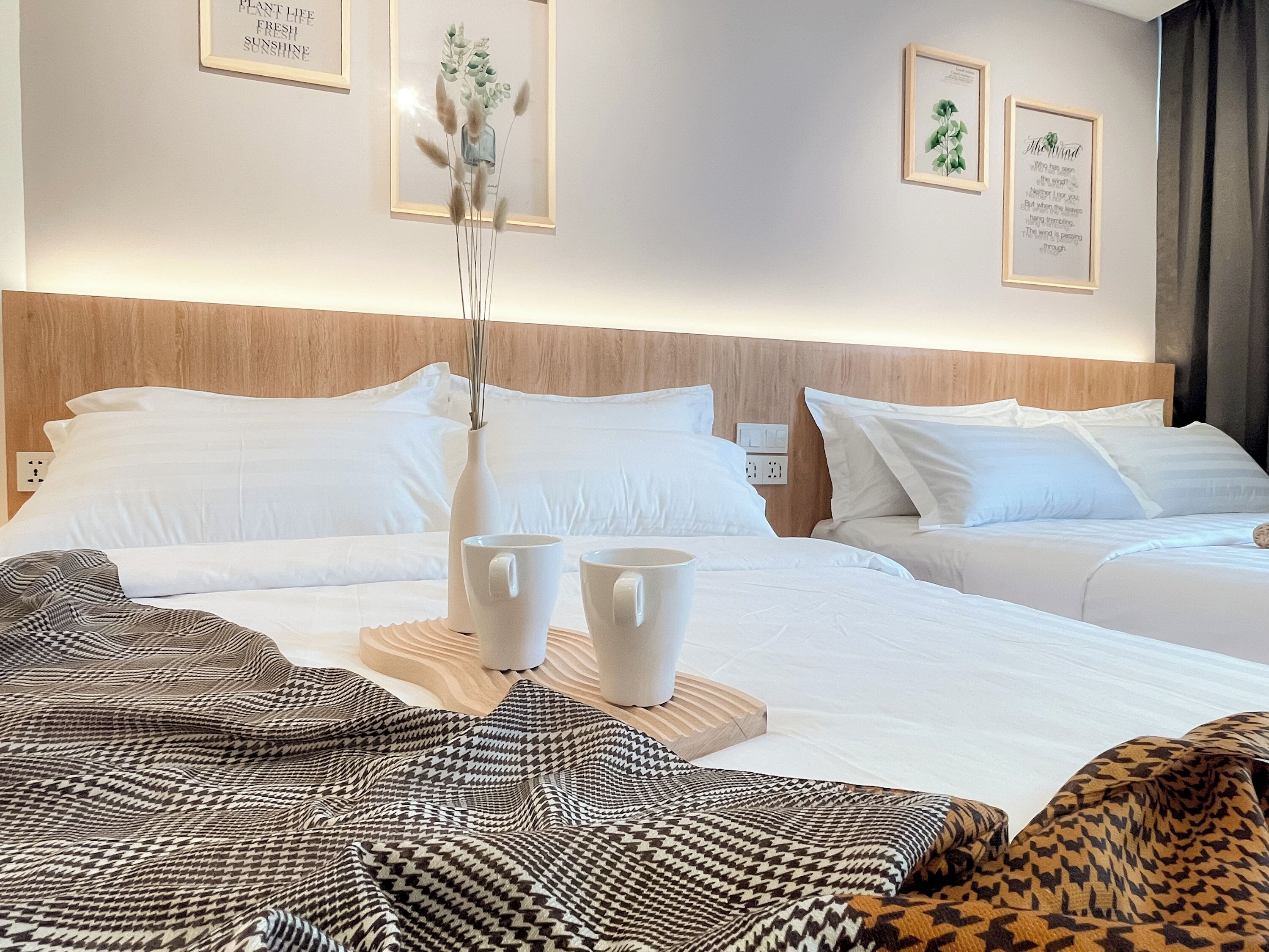 A hotel room with a wooden headboard, white bedding, and a bedside table with two white mugs.