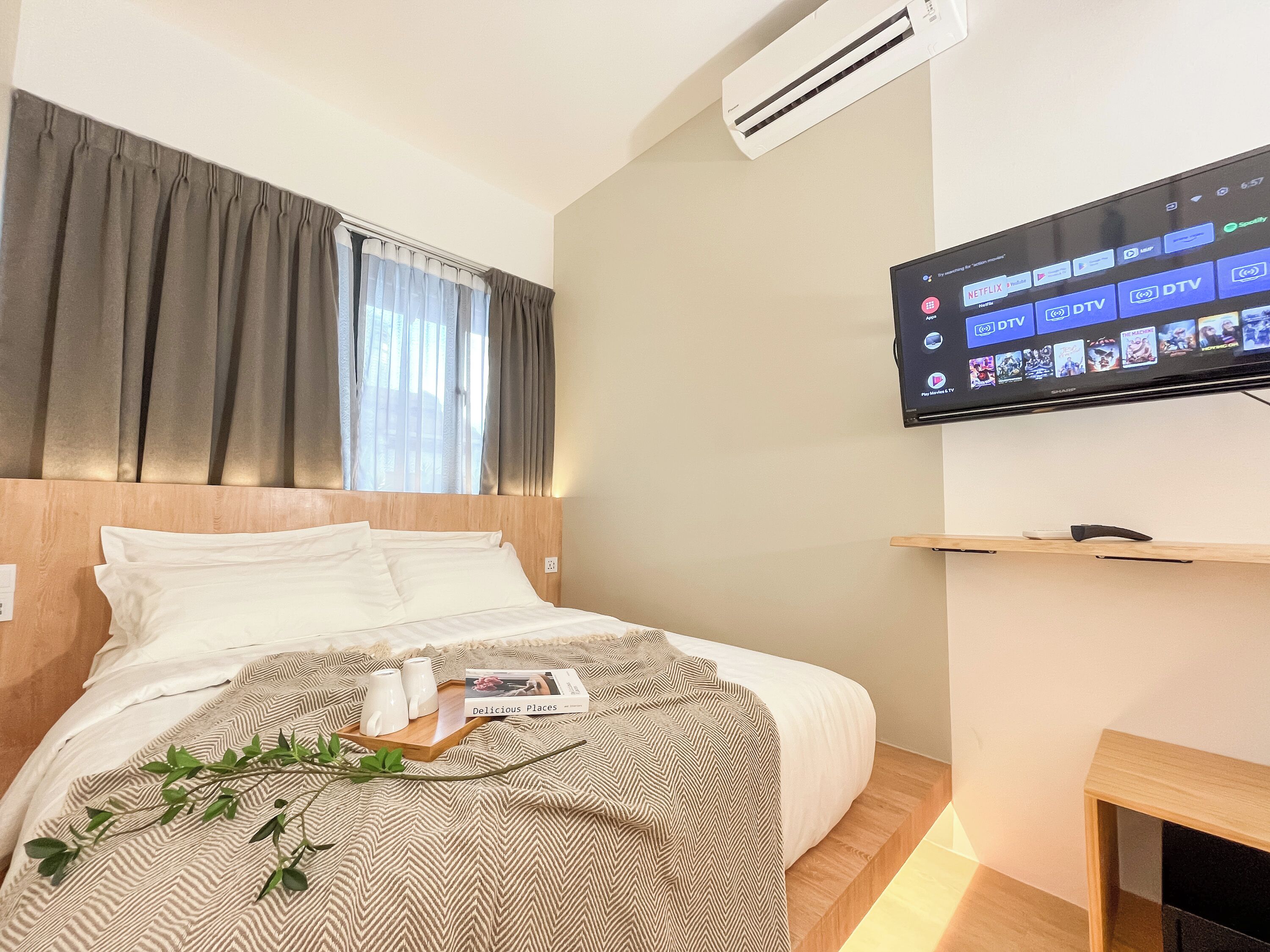 A hotel room with a bed, a TV mounted on the wall, and a window with curtains.