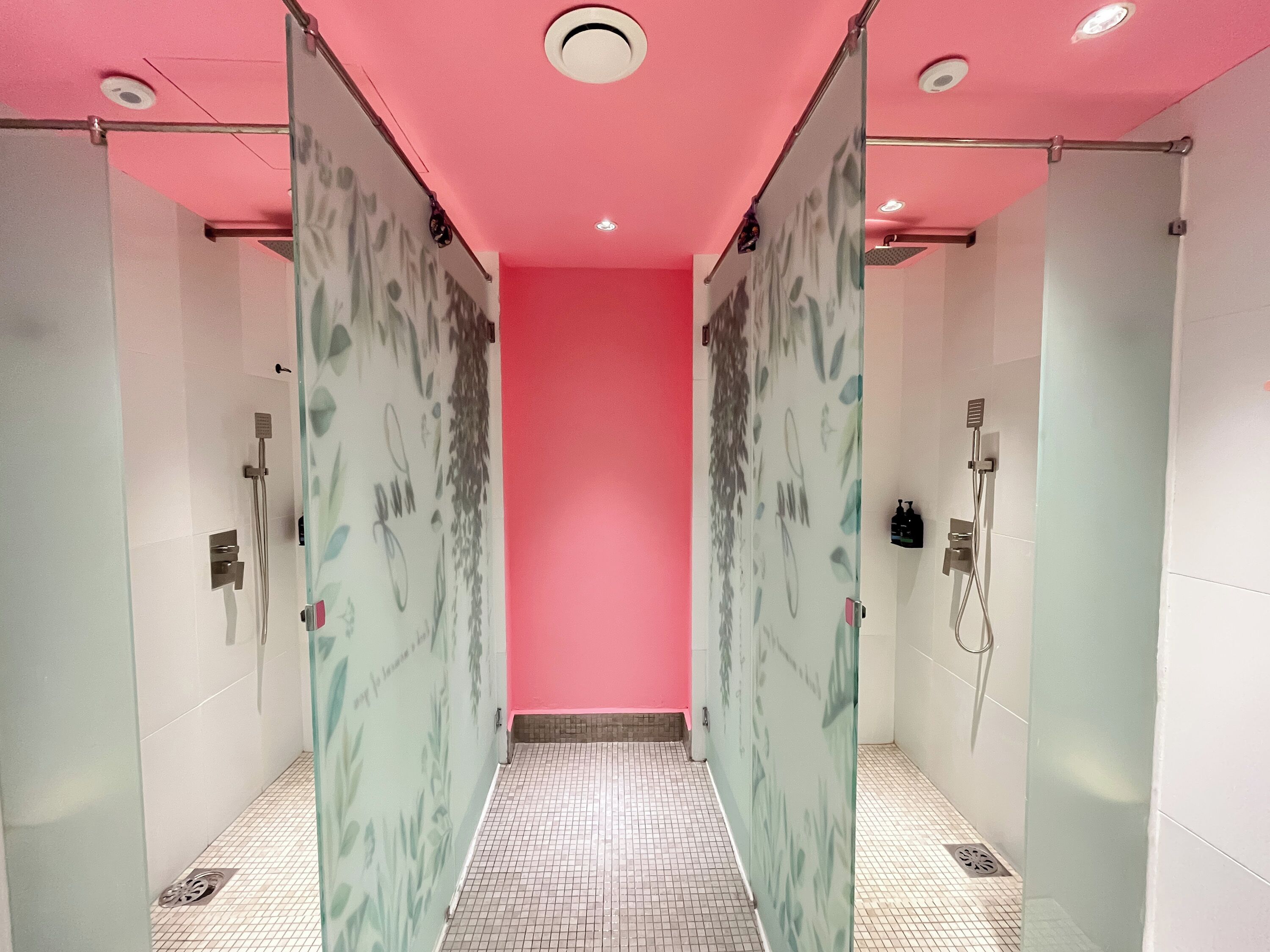 A modern bathroom with a pink wall, glass shower doors, and a tiled floor.