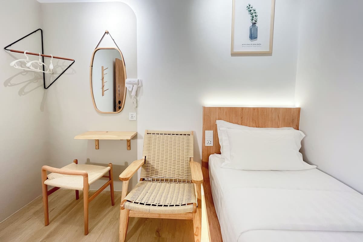 A room with a bed, a chair, a small table, a mirror, and a framed picture on the wall.