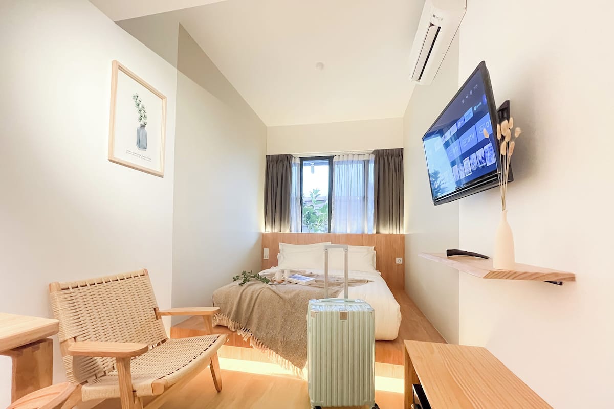 A modern hotel room with a bed, a desk, a chair, a TV, and a window with curtains.