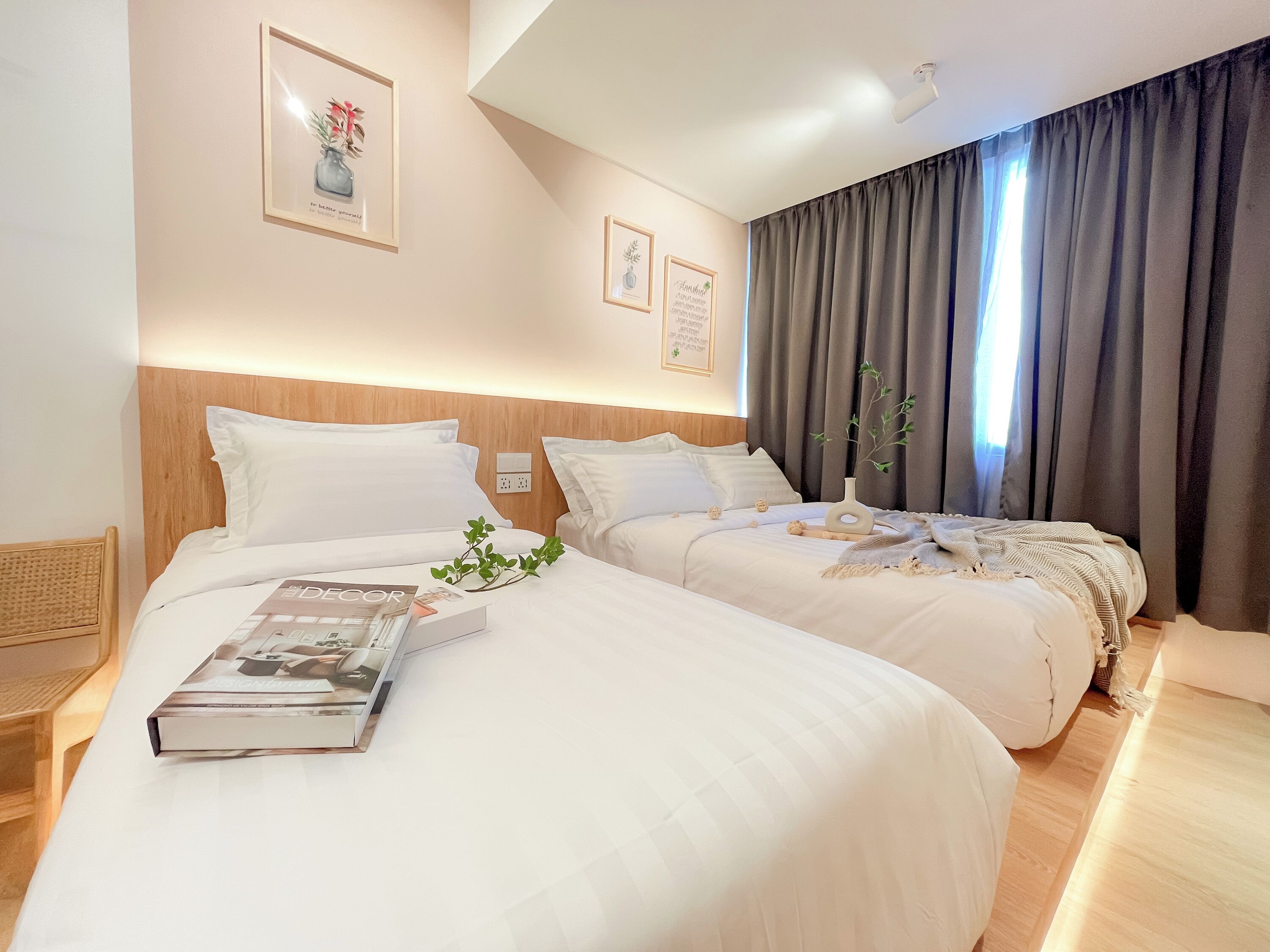 A hotel room with two beds, a wooden headboard, a bedside table with a magazine, and a window with curtains.